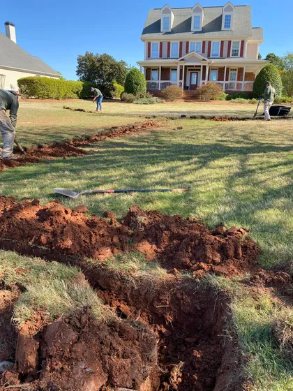 French drain trench installation across the front lawn of a large brick colonial home