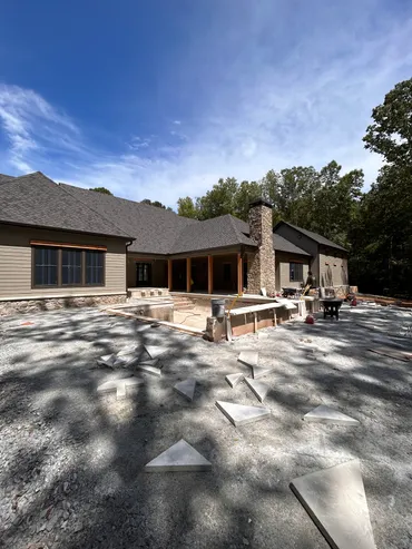 Large outdoor living area under construction with stone fireplace, pool surround, and flagstone pavers