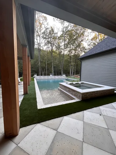 Luxury rectangular pool with attached spa and artificial turf surround, viewed from under a covered porch