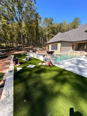 Canelo Landscape & Design crew installing artificial turf beside a luxury pool with stone fire bowls and travertine deck